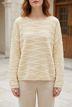Model wearing the Aurore pale cream textured knit sweater in a stone courtyard